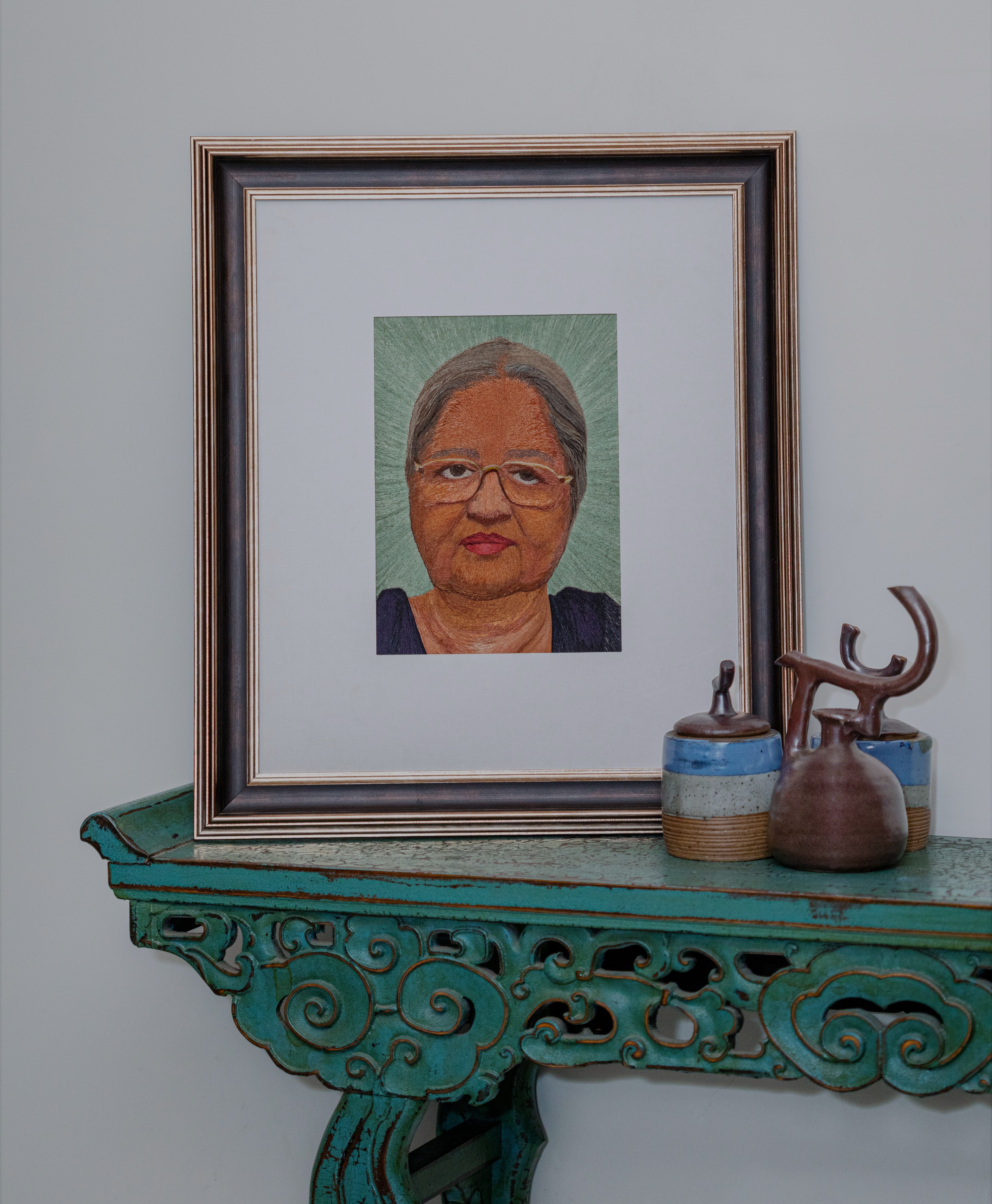 The subject is an 80 year-old woman in her reading glasses. The transparency of reading glasses and grey tones of the hair in embroidery showcases how ageing comes with its own grace

The greys in skin tones have been offset by a deep blue and aqua green background.